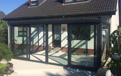 Dunkler Glasanbau mit großen Fenster- und Türelementen an einem Wohnhaus