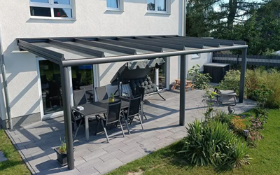 Moderne Terrassenüberdachung aus dunklem Aluminium und Glas an einem Wohnhaus mit Garten
