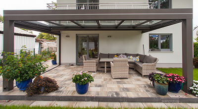 Terrasse mit flachem Glasdach mit Gartenmöbeln und Blumen