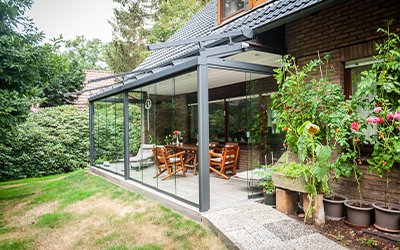 Verglaster Sommergarten mit grauen Aluminiumprofilen und Sitzbereich an einem Backsteinhaus