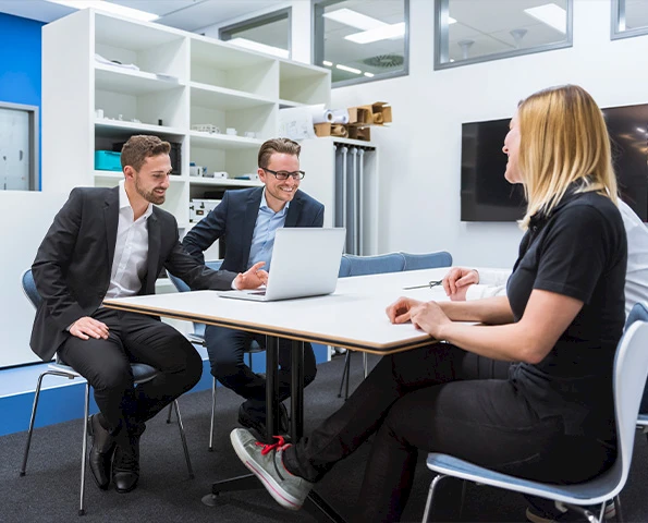 Beratungsgespräch im modernen Büro, drei Personen besprechen Projekt am Laptop, professionelle Kundenberatung.