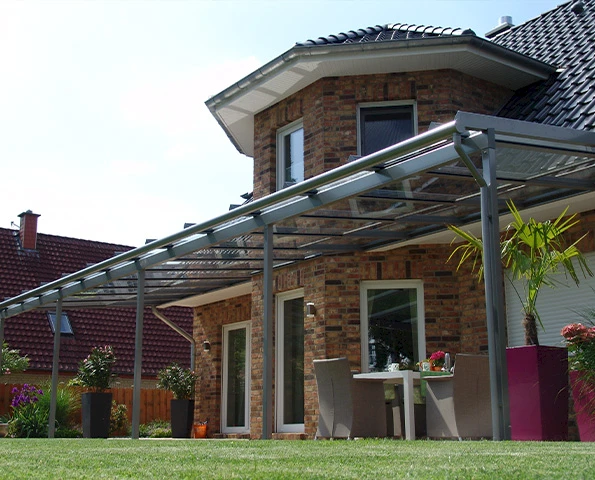 Terrassenüberdachung aus Glas und Aluminium als eleganter Wetterschutz am Haus.