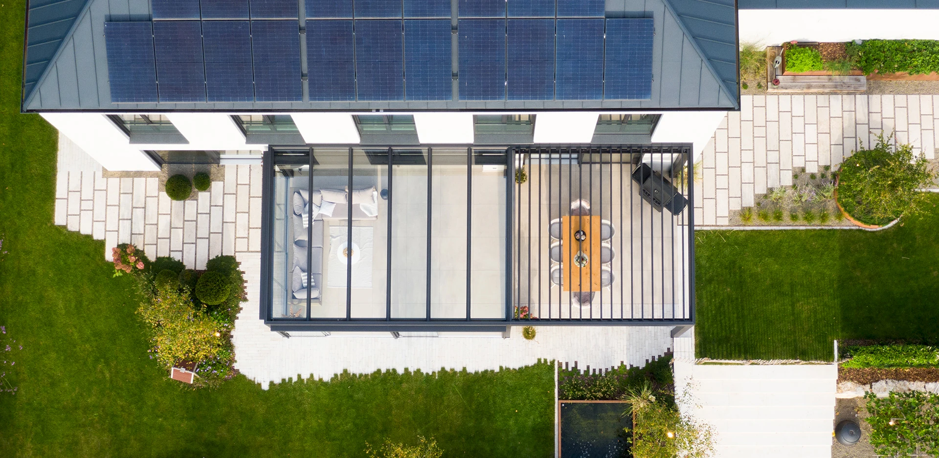 Lamellendach mit Glasdach-Kombination an einem modernen Wohnhaus, aufgenommen aus der Vogelperspektive mit Blick auf Terrasse und Garten