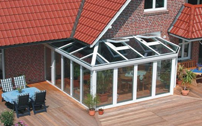 Moderner Wintergarten mit weißen Aluminiumprofilen und Glasdach, angrenzend an eine große Holzterrasse.