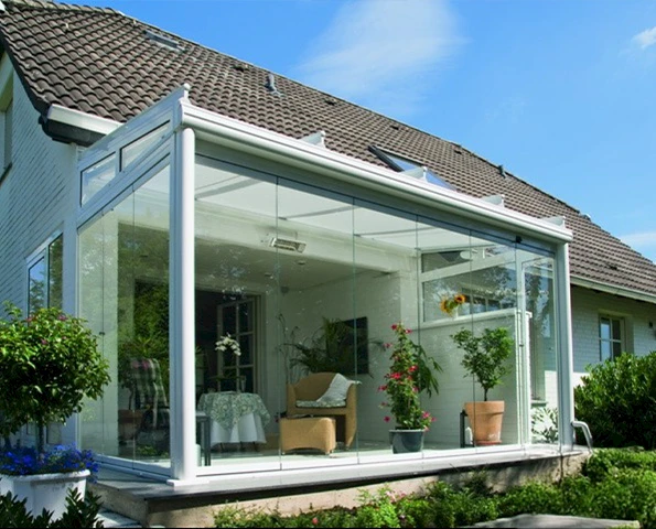 Moderner Sommergarten mit rahmenlosen Glasschiebetüren und weißen Aluminiumprofilen, angebaut an ein Einfamilienhaus mit Garten und Sitzbereich.