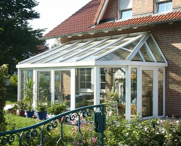 Klassischer Wintergarten mit Glas-Satteldach, weißen Profilen und üppiger Bepflanzung im Vorgarten.
