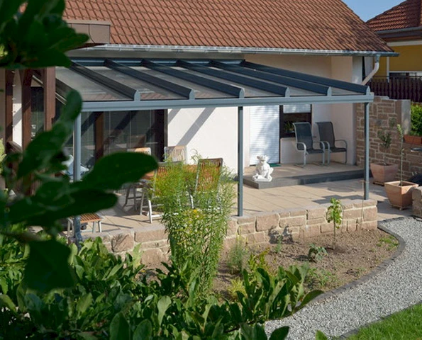 Filigrane Aluminium-Terrassenüberdachung mit Glasdach über einer gemütlichen Sitzecke im Garten.