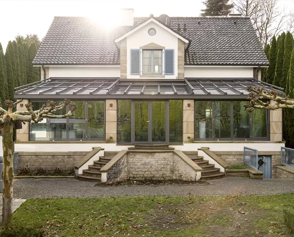 Großzügiger Wintergarten mit Aluminiumprofilen an einer Villa im Landhausstil mit Treppen und Gartenblick.