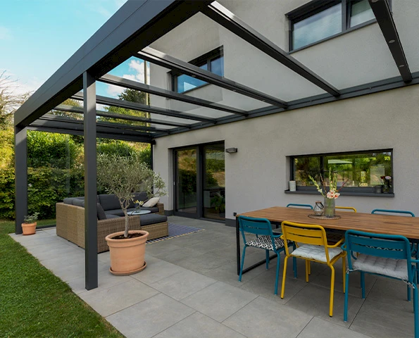 Filigrane Aluminium-Terrassenüberdachung mit Glasdach über einer modernen Sitzgruppe im Garten.