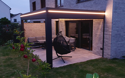 Modernes Terrassendach mit LED-Lichtband an einem Einfamilienhaus und gemütlicher Sitzecke im Garten.