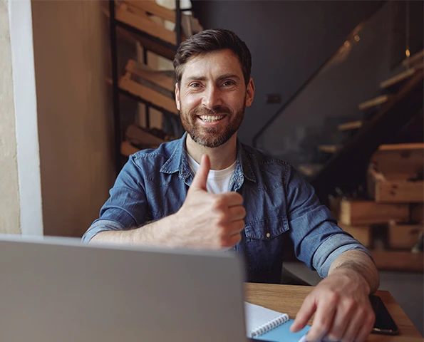 Zufriedener Kunde am Laptop zeigt Daumen hoch nach erfolgreicher Beratung oder Projektfreigabe.