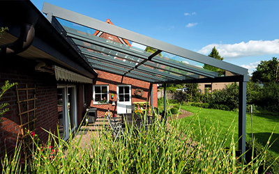 Moderne Terrassenüberdachung mit Glasdach und weißem Aluminiumgestell über einer großzügigen Terrasse.