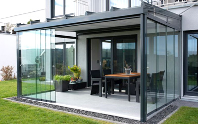 Kleiner Sommergarten mit Glaswänden als geschützter Sitzbereich im Garten