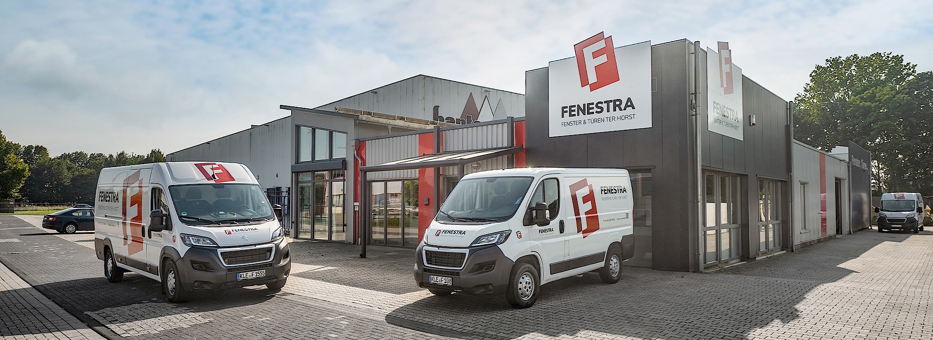 Außenansicht des Firmengebäudes von Fenestra mit Firmenlogo und beschrifteten Servicefahrzeugen.