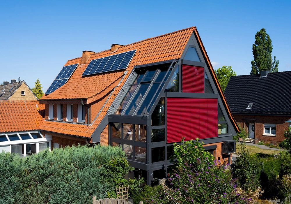 Großer Wintergarten mit Glasdach und roter Außenbeschattung an einem Wohnhaus mit Solarpaneelen