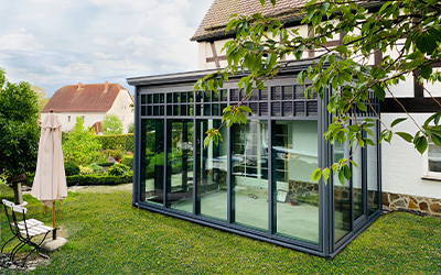 Moderner Wintergarten Anbau mit Glas-Schiebeelementen und Aluminiumrahmen im Garten.