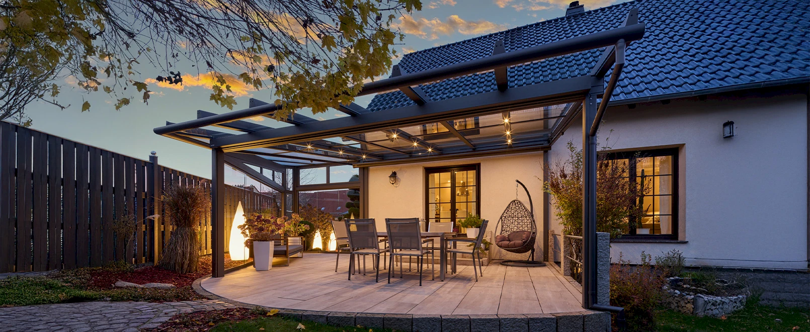Terrassenüberdachung mit Glasdach und integrierter Beleuchtung bei Abendstimmung