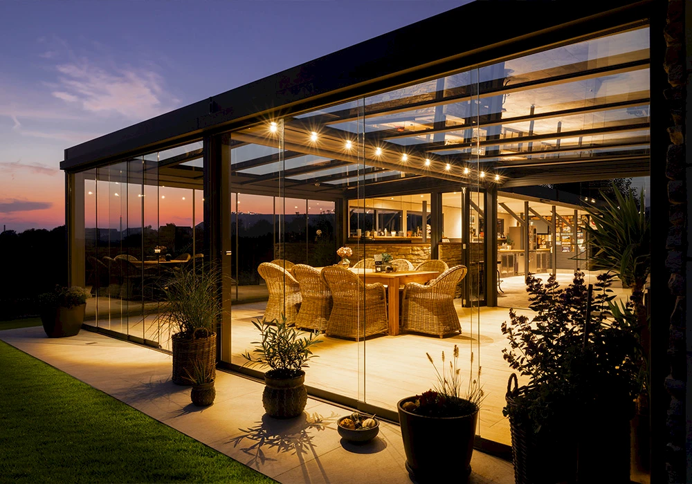 Exklusiver Sommergarten mit Glaswänden und stimmungsvoller Beleuchtung bei Sonnenuntergang