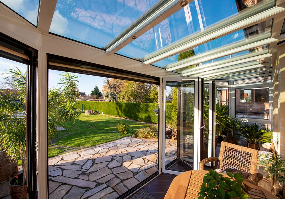Heller Wintergarten mit Glasdach und geöffneten Glasfaltwänden, Blick auf Terrasse und grünen Garten.