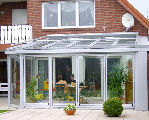 Wintergarten aus Aluminium und Glas mit Flachdach, angebaut an ein Einfamilienhaus mit Klinkerfassade.
