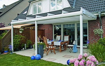 Terrassenüberdachung mit weißem Aluminiumrahmen und integrierter Markise über einem gemütlichen Essbereich.