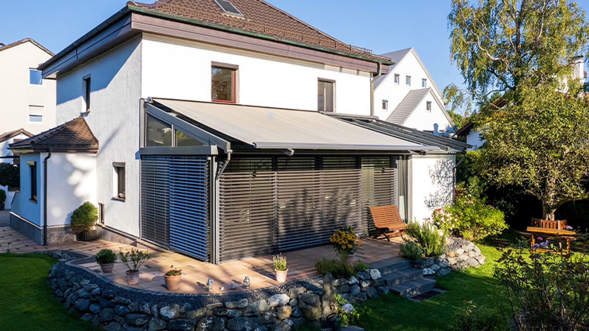 Wintergarten mit ausgefahrener Dachmarkise und seitlicher Beschattung im Garten