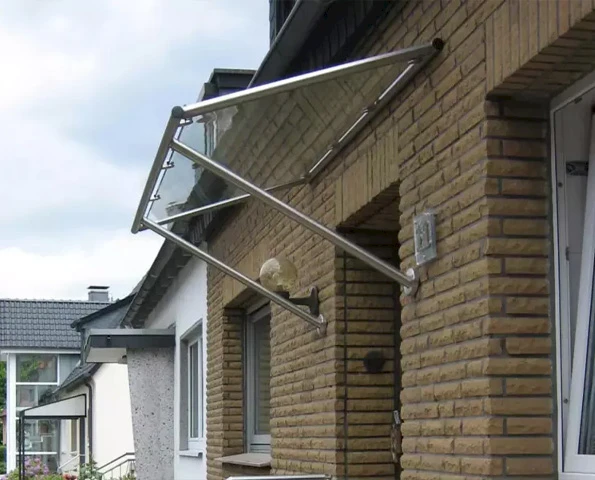 Glasvordach mit Edelstahlträgern über Eingangstür, stilvoller Wetterschutz mit klarer Linienführung.