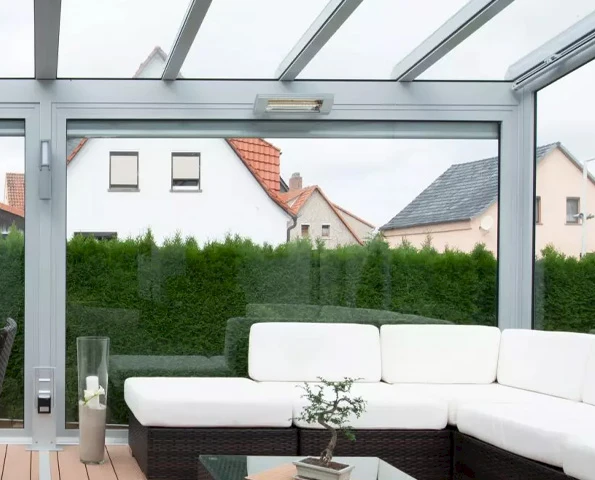 Wintergarten mit Glasdach und Infrarot-Heizstrahler, moderne Lounge mit weißem Sofa und klarer Sicht nach draußen.