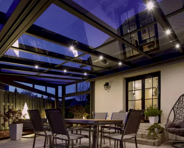 Terrassenüberdachung mit integrierter LED-Beleuchtung am Abend, gemütlicher Essbereich im Außenbereich.