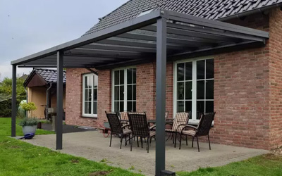 Anthrazitfarbene Aluminium-Terrassenüberdachung mit Glasdach an Klinkerhaus, gemütlicher Sitzplatz im Garten.
