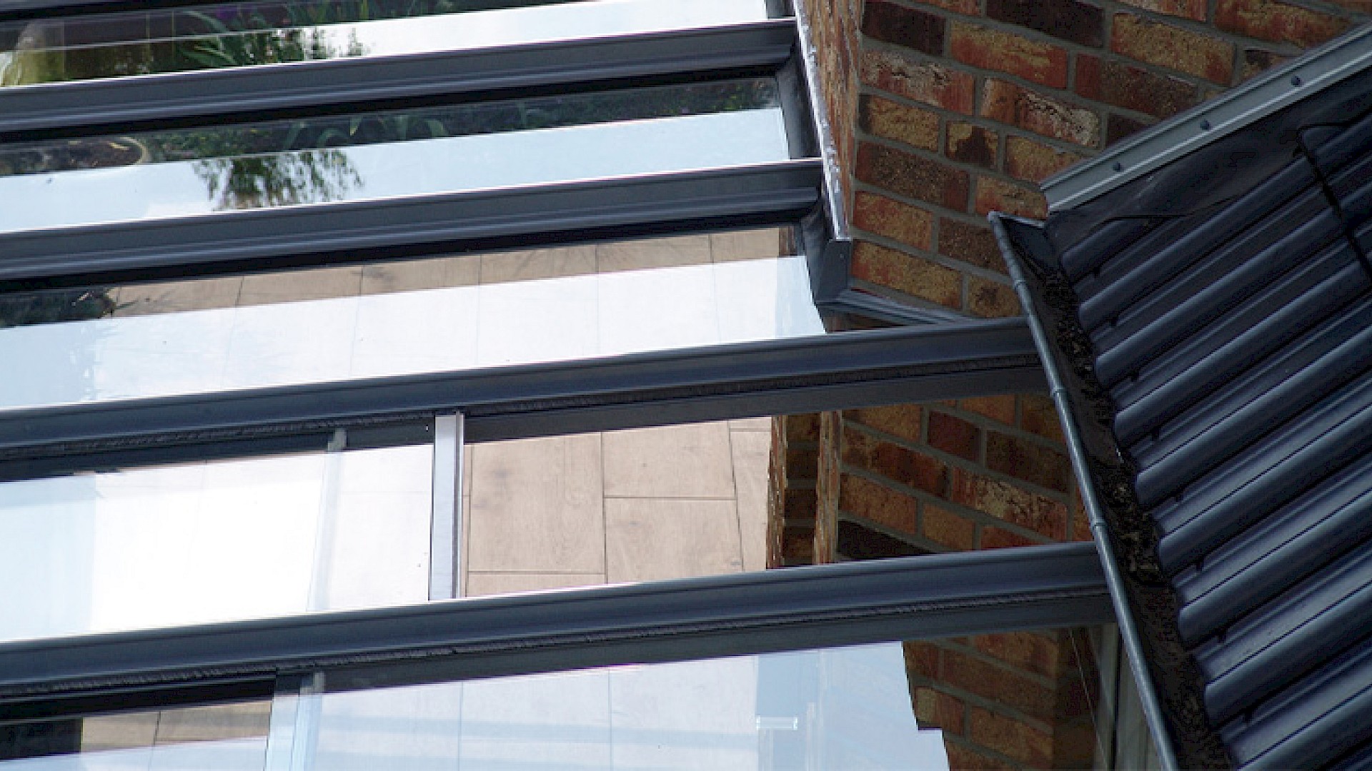 Detailaufnahme einer Terrassenüberdachung mit Glasdach und integrierter Belüftung am Hausanschluss