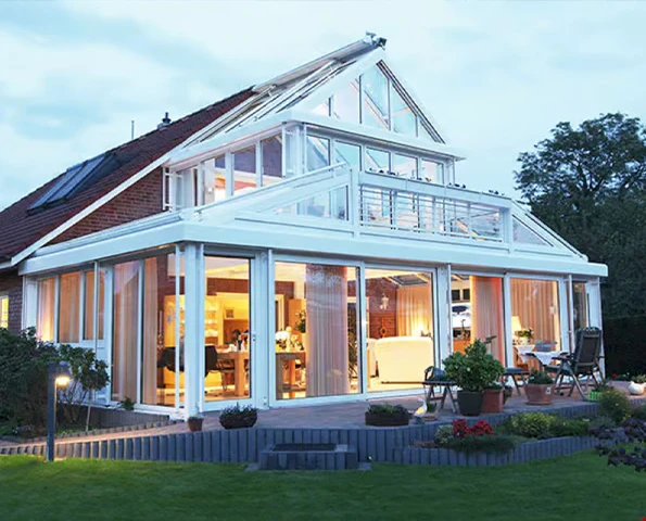 Großer Wintergarten mit doppelter Glasfassade und Galerieebene, beleuchteter Wohnbereich im Abendlicht.