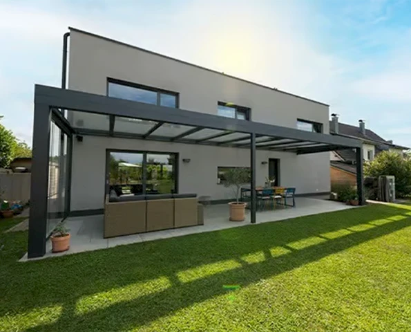 Geradlinige Terrassenüberdachung aus Aluminium mit Glasdach, angebaut an modernes Wohnhaus mit Garten.