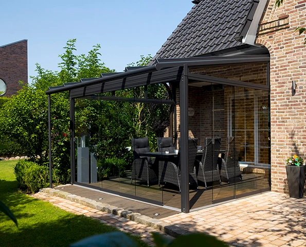 Sommergarten mit rahmenloser Verglasung und stilvoller Einrichtung, stimmungsvoll beleuchtet in der Dämmerung.