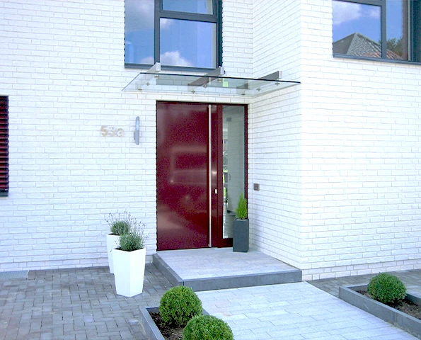 Glasvordach mit Edelstahlträgern über Eingangstür, stilvoller Wetterschutz mit klarer Linienführung.