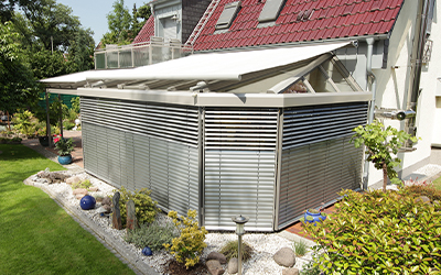Wintergarten mit außenliegenden Lamellen und Markise als Sonnen- und Sichtschutz an einem Einfamilienhaus.
