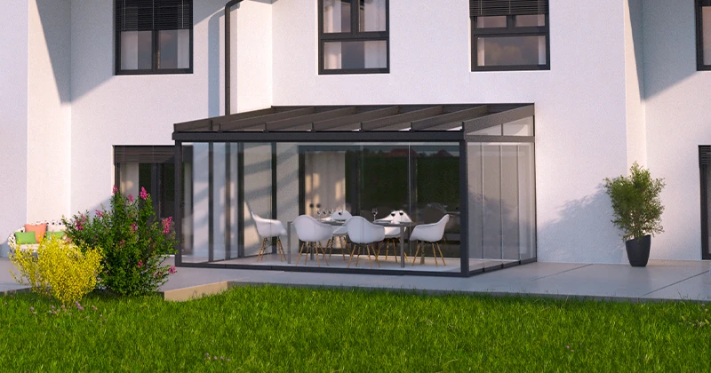 Sommergarten mit außenliegendem Sonnenschutz in dezentem Grau, großzügig verglast und mit stilvollem Esstisch und schwarzen Stühlen ausgestattet.