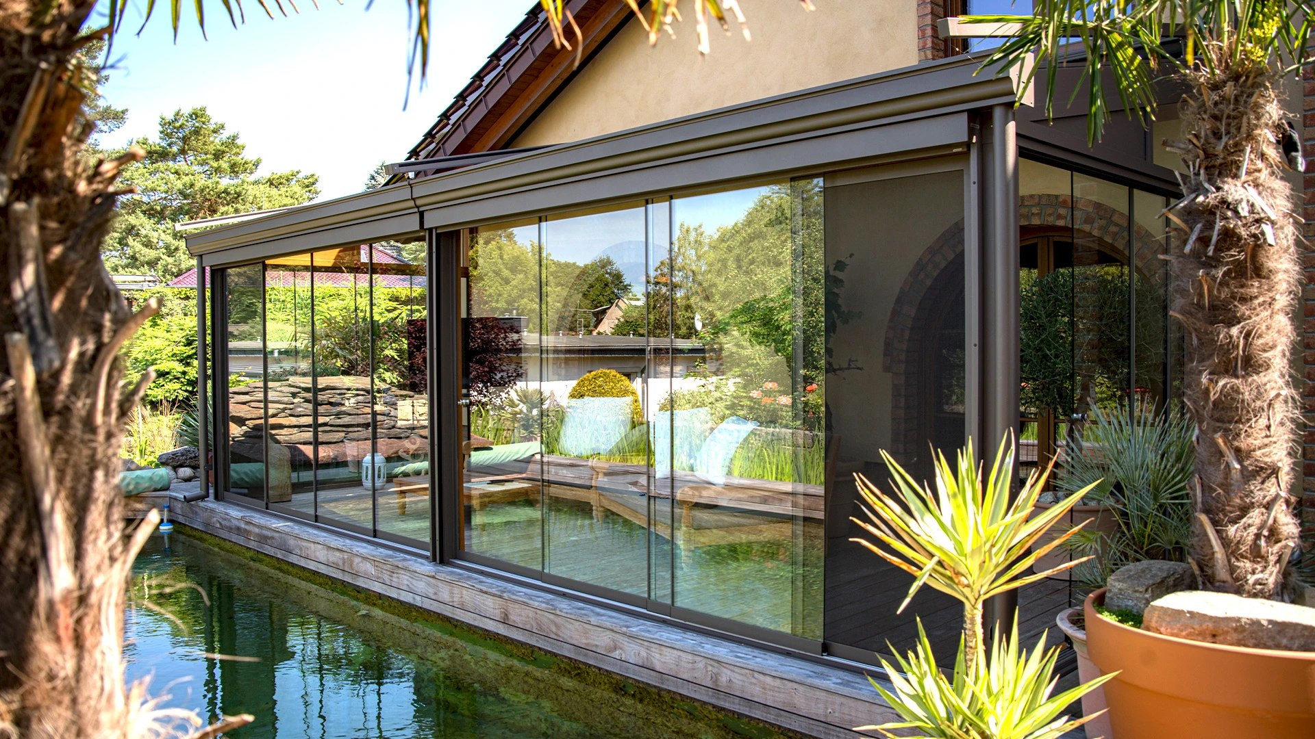 Sommergarten mit Glas-Schiebetüren direkt am Teich – ganzjähriger Wohnkomfort im Grünen.