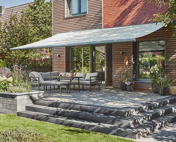 Hochwertige Markise als Sonnenschutz über moderner Terrasse mit Sitzgruppe und Gartenblick.
