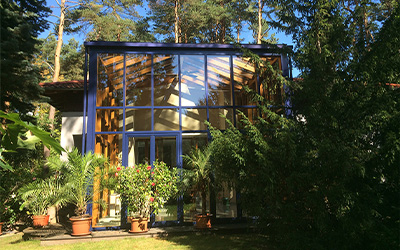 Wintergarten mit großer Glasfassade und Holzelementen, eingebettet in einen grünen Garten.