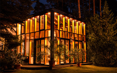 Beleuchteter Wintergarten mit Glasfassade und Holzrahmen – stimmungsvoller Wohnraum bei Nacht.