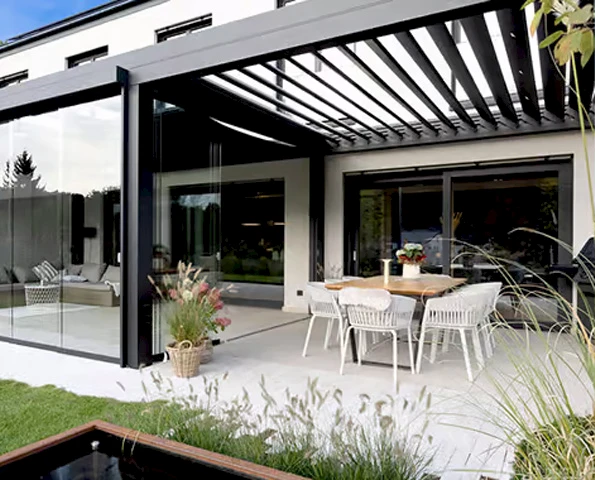Modernes Lamellendach aus Aluminium mit seitlichen Glasschiebetüren und stilvollem Essbereich im Garten.