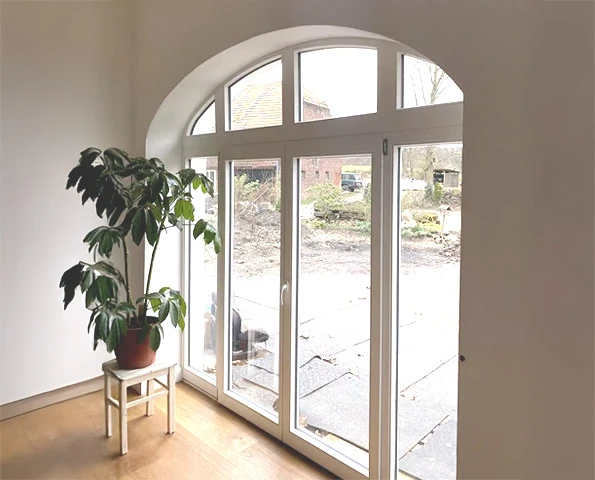 Großes weißes Rundbogenfenster mit Doppeltür und Blick in den Garten, heller Wohnraum mit Zimmerpflanze.