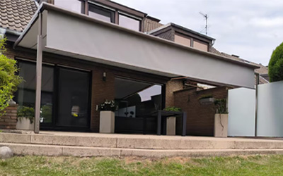 Moderne Terrassenüberdachung mit integrierter Senkrechtmarkise als Sicht- und Sonnenschutz an einem Einfamilienhaus.