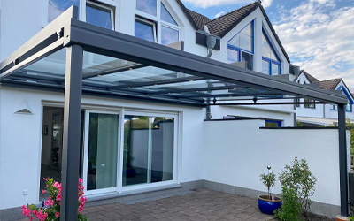 Anthrazitfarbene Aluminium-Terrassenüberdachung mit Glasdach und offenem Terrassenbereich am modernen Wohnhaus.