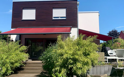 Rote Fassadenmarkise als stilvoller Sonnenschutz für Terrasse und Garten eines modernen Wohnhauses.