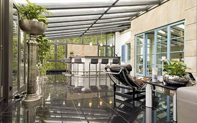 Innenansicht eines modernen Wintergartens mit Glasdach, schwarzen Fliesen und stilvoller Einrichtung.