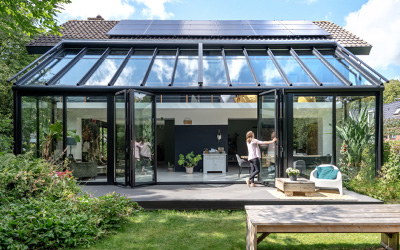 Wintergarten mit vollständig öffnbaren Glaswänden und Solarpaneelen auf dem Dach, Blick in den Garten.