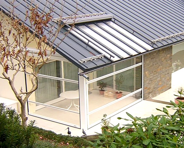 Moderner Wintergarten mit weißen Aluminiumprofilen, großem Glasdach und angrenzender Steinwand.