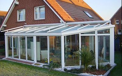 Großer Wintergarten mit weißen Aluminiumprofilen und Glasflächen, direkter Zugang zum Gartenbereich.